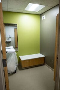 Changing room to MRI center with small bench on back wall with mirror adjacent and dirty clothes hamper underneath.