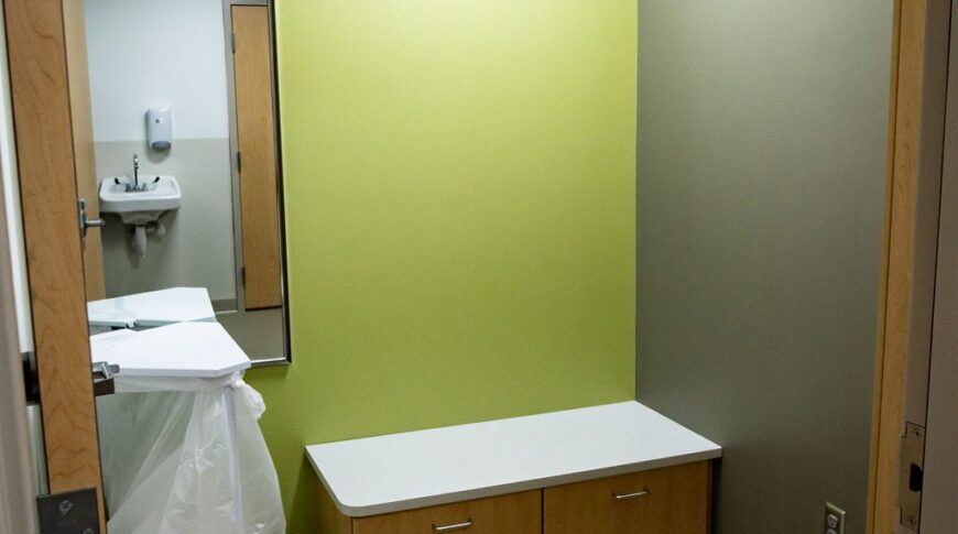 Changing room to MRI center with small bench on back wall with mirror adjacent and dirty clothes hamper underneath.