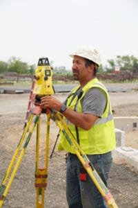 Comstock Construction site superintendent wearing yellow vest and white hard hat looking through surveying kit.