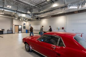 Mechanic bay at Dunseith CTE Center with red hot rod car and students in the background. Photo by Icon Architectural Group.