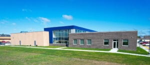 Exterior aerial view of a CTE center with brown brick section on the right, blue accented facade with full windows in the center, and beige precast concrete to the left. Photo by Icon Architectural Group.