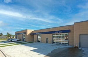 Exterior of CTE school with four large garage bays with full-window doors and a blue ribbon above each with a label for which shop it is. Photo credit to Icon Architectural Group.