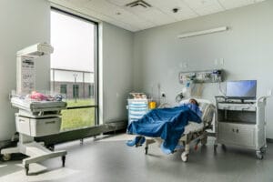 Maternity care room simulator with mother medical manikin on hospital bed and baby manikin under heating lamp station.