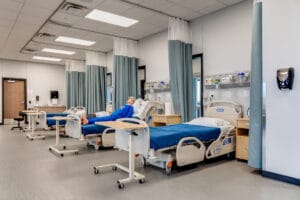 Hospital simulation room with patient bed stations and dividing curtains spanning the length of the room.