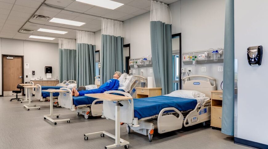 Hospital simulation room with patient bed stations and dividing curtains spanning the length of the room.