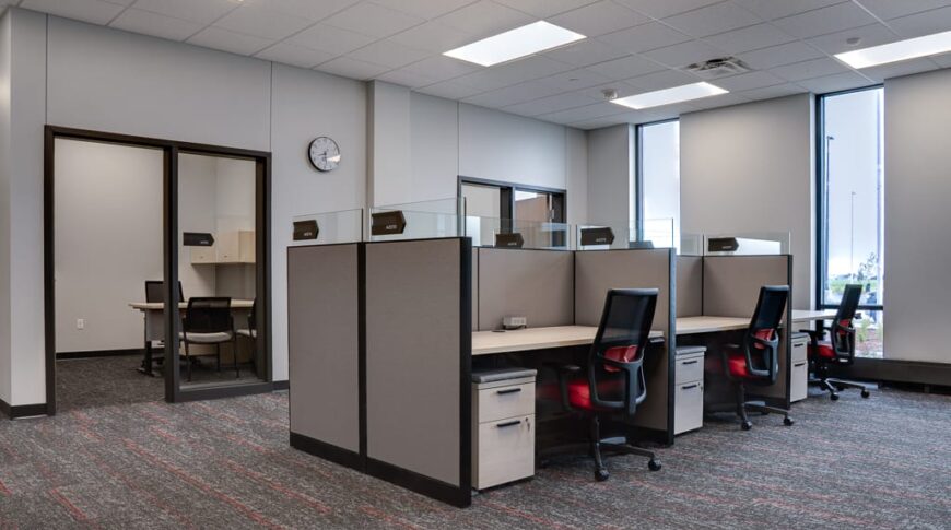 Cubicle workstations in the middle of an office space surrounded by office rooms.