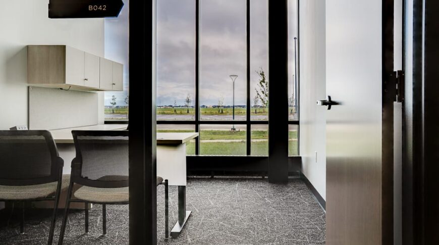Modern office with workstation and two chairs to the right with floor to ceiling windows overlooking the grounds.