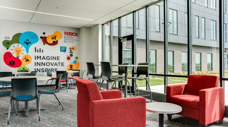 Commons area at NDSCS Career Innovation Center with bright red seating char area in front with round tables and chairs in background. Brightly colored mural on back wall that says "Imagine. Innovate, Inspire." Wall of floor to ceiling windows to the right.