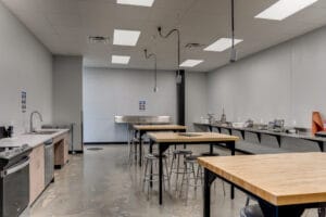 Meat processing classroom complete with kitchen workstation along the left wall, processing equipment on the right wall, and bar-height tables and stools in the center.