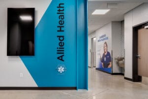 Hallway view of entrance to nursing wing with a bright blue graphic and the words "Allied Health" painted on it. Another graphic a little ways further down the hall alongside a water fountain station.