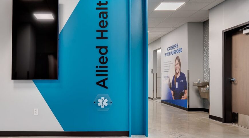 Hallway view of entrance to nursing wing with a bright blue graphic and the words "Allied Health" painted on it. Another graphic a little ways further down the hall alongside a water fountain station.