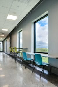 Interior hallway with large windows overlooking landscaping with countertop and chairs station underneath to work.
