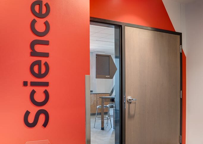 Bright red painted wall that says "Science" with a door and window besides that leads to the science wing of the school.