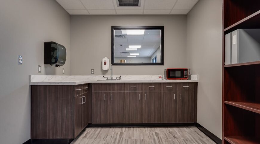 Breakroom kitchenette with sink and microwave and some dark walnut laminated cabinets.