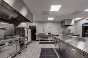 Industrial kitchen with stainless steel island to the right and appliances to the left. Wash station to the back wall.