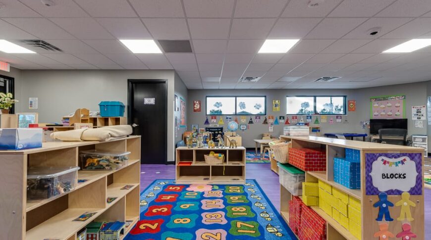Kids playroom with waist-height storage shelves on either side, a brightly-colored numbers rug underneath and toys all around.