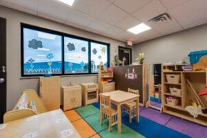 Playroom area with light birch wood playhouse equipment overlooking outside through three windows.