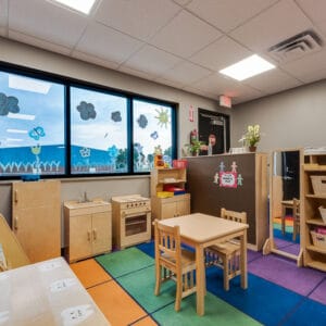 Playroom area with light birch wood playhouse equipment overlooking outside through three windows.