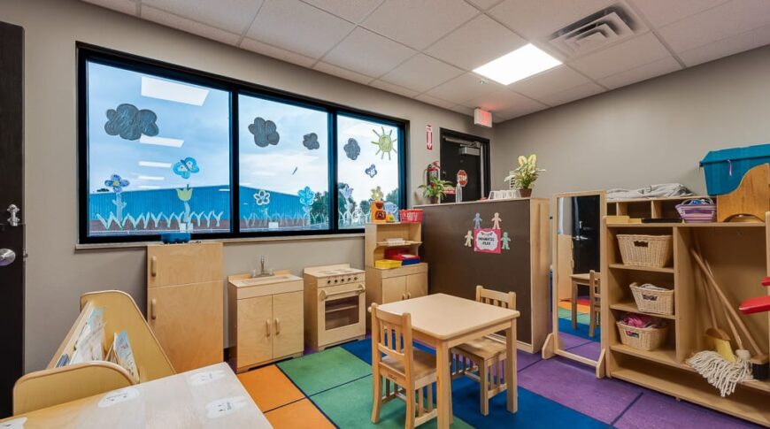Playroom area with light birch wood playhouse equipment overlooking outside through three windows.