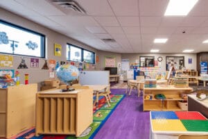 Large kids playroom with purple laminate flooring and light birch colored storage and play equipment and tables throughout for the children at Enemy Swim Head Start.