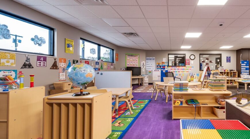 Large kids playroom with purple laminate flooring and light birch colored storage and play equipment and tables throughout for the children at Enemy Swim Head Start.