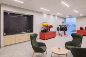 Sitting area with three green wingback chairs and table in the middle. Convenient kitchenette station behind to the left with farm implements on display on the back right.
