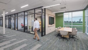 Row of STARC office walls of floor-to-ceiling windows with a hallway leading to the left. Open-air small conference area with table and chairs and monitor to the back right.