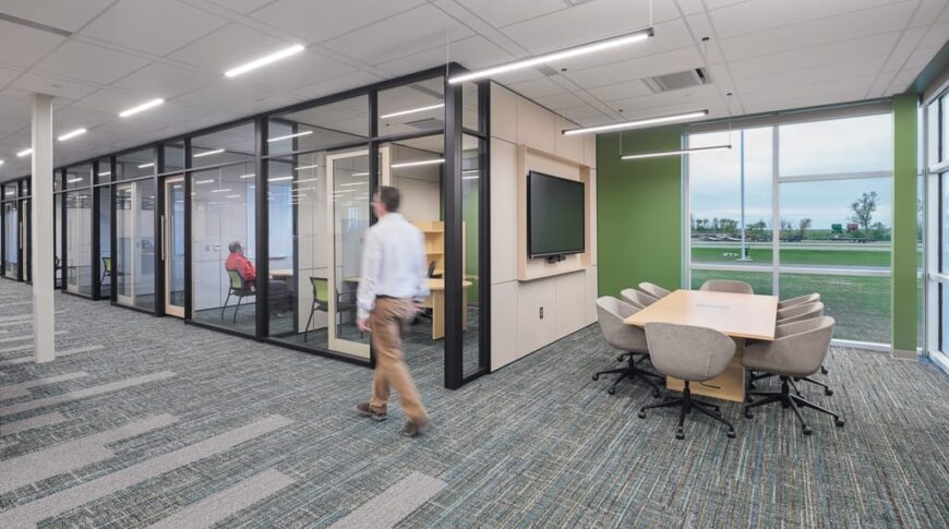 Row of STARC office walls of floor-to-ceiling windows with a hallway leading to the left. Open-air small conference area with table and chairs and monitor to the back right.