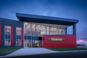 Close-up exterior nighttime image of the gray and red Vaderstad precast building.