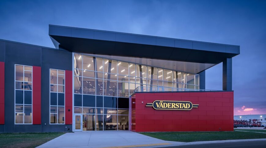 Close-up exterior nighttime image of the gray and red Vaderstad precast building.