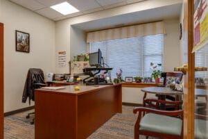 Newly constructed office space with large cherrywood L-shaped desk and two chairs with large window behind.