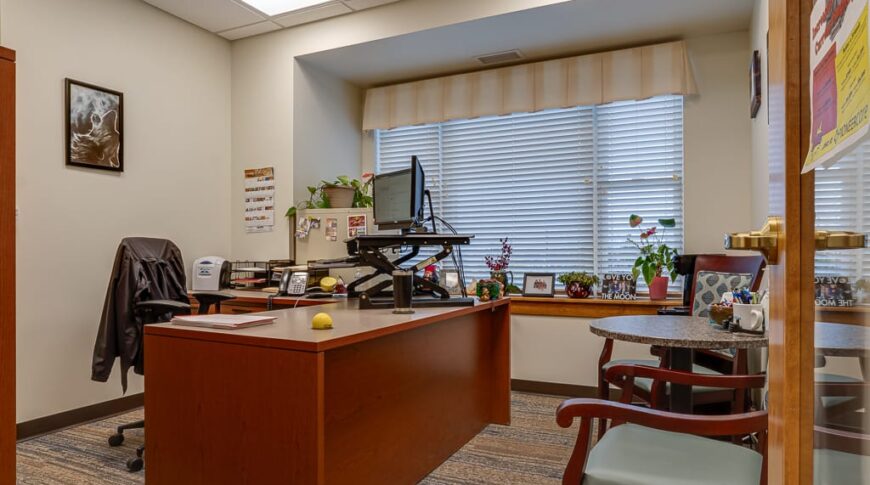 PioneerCare-Low Res-2 Newly constructed office space with large cherrywood L-shaped desk and two chairs with large window behind.
