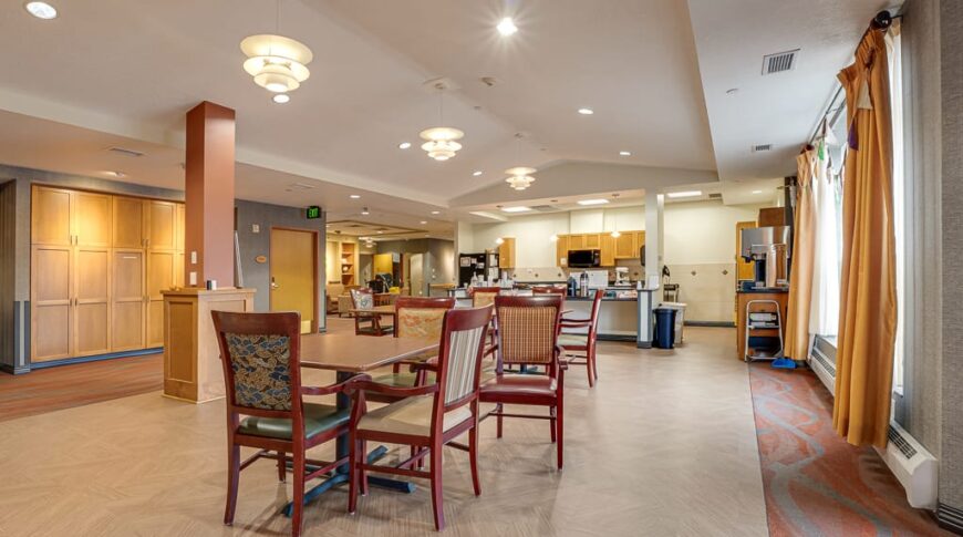 PioneerCare-Low Res-67 Newly done laminate flooring in nursing home dining rom with tables and chairs throughout and bright big windows overlooking the grounds.