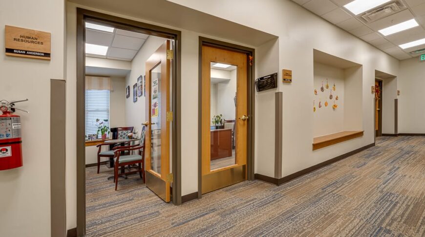PioneerCare-Low Res-7 Hallway to new office addition at PioneerCare Center in Fergus Falls, MN. Two windowed doors down the hallway with a large nook built into the wall for artwork.