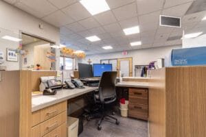 Receptionist station with light-colored wood grained cabinetry, fitted with double monitors and phones.