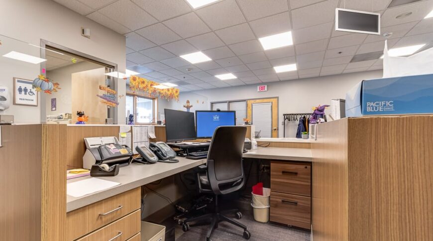 Sanford Hillsboro-Low Res-18 Receptionist station with light-colored wood grained cabinetry, fitted with double monitors and phones.