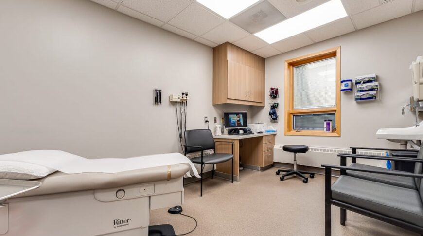 Sanford Hillsboro-Low Res-23 Patient exam room with medical exam table to the left, chairs and sink station to the right and chair and doctor station to the back.
