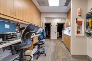 Open-air nurses station with bar-height chairs and computer stations with upper cabinetry to the left and upper and lower cabinetry to the right.