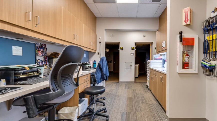 Sanford Hillsboro-Low Res-24 Open-air nurses station with bar-height chairs and computer stations with upper cabinetry to the left and upper and lower cabinetry to the right.