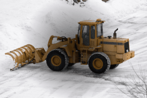 Yellow tractor snowplow clearing snow in a parking lot.