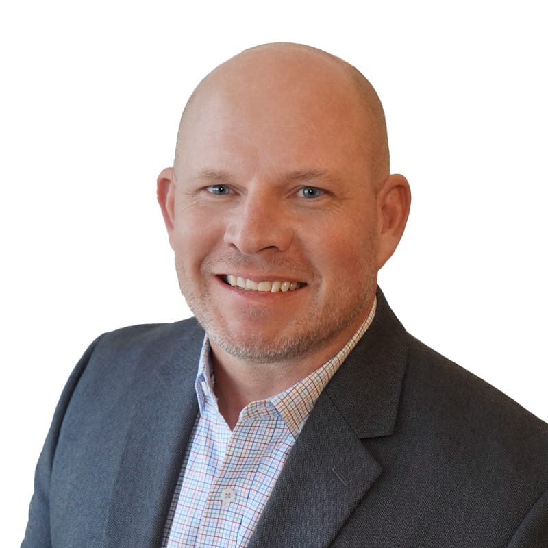 Middle-aged white man with blue eyes, scruff and shaved head wearing gray suit jacket and orange and blue plaid shirt.