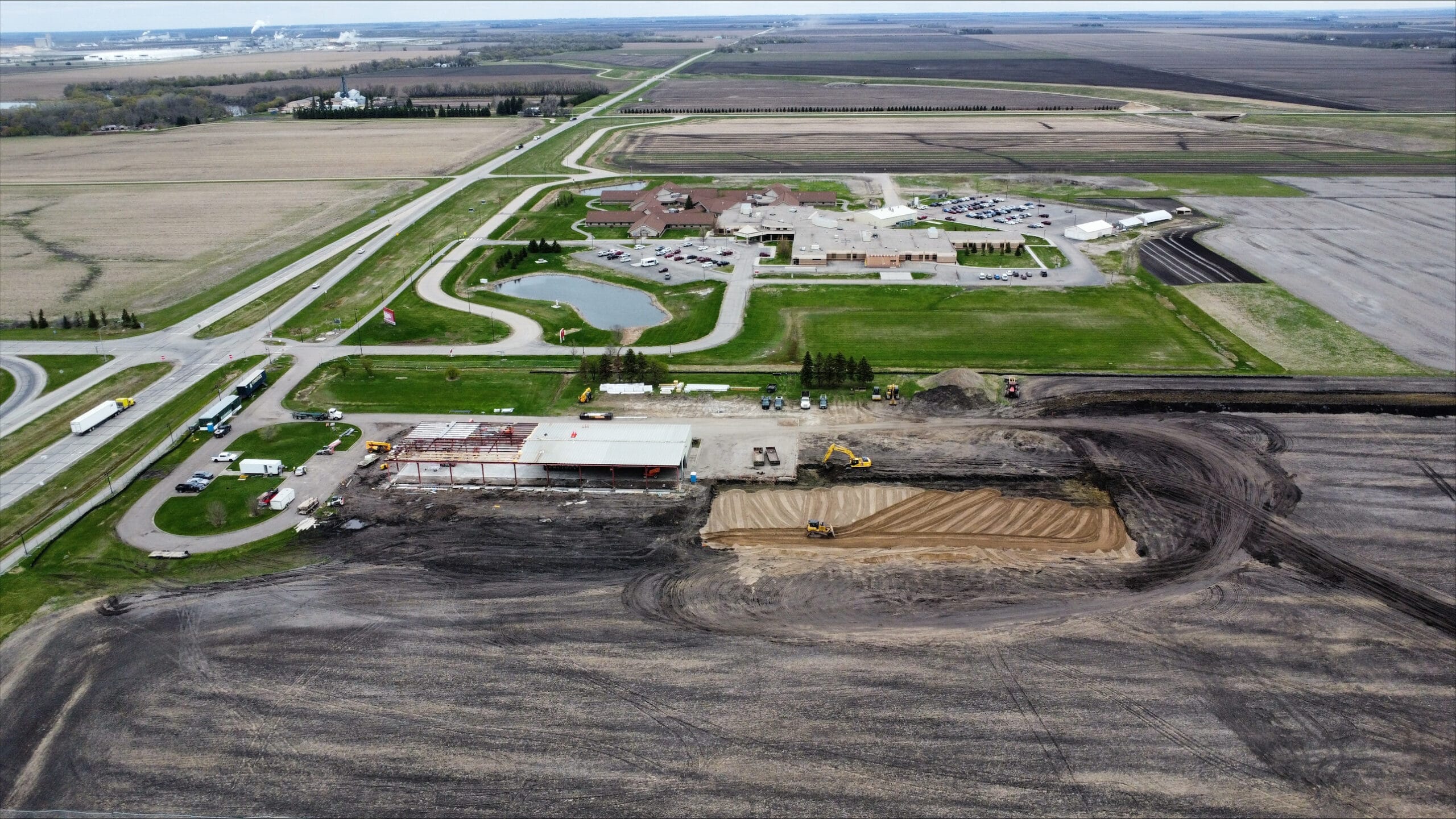 Aerial drone image showing a dirt field with construction at the site of the new Infinity Center. Mycogen building to the left and empty plot to the right. 