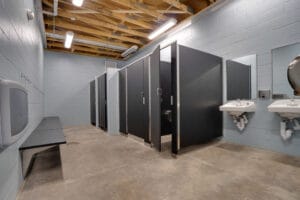 Gray bathroom/changing room with cinder block walls, concrete floor, and exposed wood rafter ceiling.