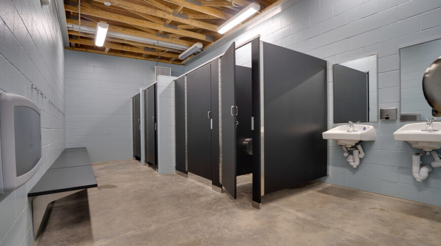 Gwinner Aquatic Center-Low Res-23 Gray bathroom/changing room with cinder block walls, concrete floor, and exposed wood rafter ceiling.