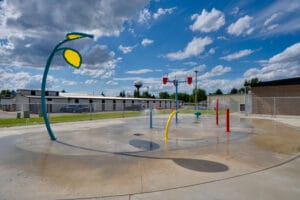 Colorful outdoor splash-pad with concrete flooring and blue skies behind.