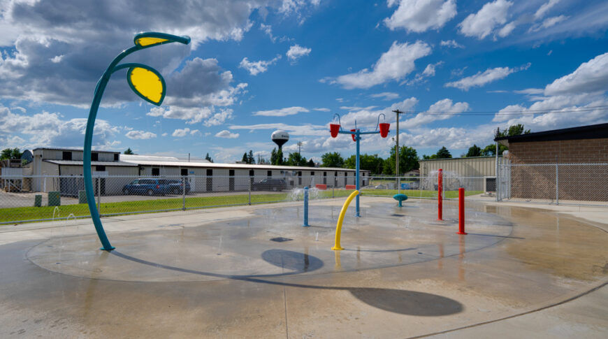 Gwinner Aquatic Center-Low Res-28 Colorful outdoor splash-pad with concrete flooring and blue skies behind.