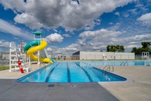 Gwinner Aquatic Center swimming pool from deep end viewpoint with lifeguard stand and waterslides to the left and basketball hoop to the right.