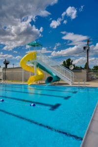 Outdoor swimming pool with two waterslides and blue skies behind.
