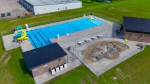Aerial view of the new Gwinner Aquatic Center with concessions and bathhouse to the right, splash pad besides, mechanic building to the bottom and pool to the top.