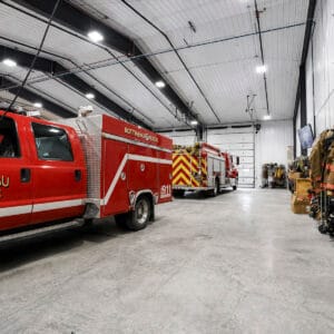 Interior of Bottineau Fire Hall with prefabricated metal building, concrete floors, fire trucks and shelves of firefighters clothing.